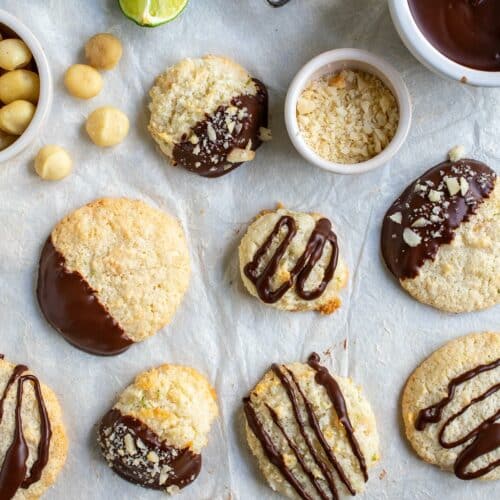 Flat lay of lots of dairy free macaroons both flat ones and puffy ones dipped and drizzled with a cooling rack and limes and a bowl of ganache plus macadamia nuts.