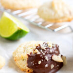 Pinterest image with a close-up of a one chocolate dipped macaroon with other cookies in the background and a lime quarter.