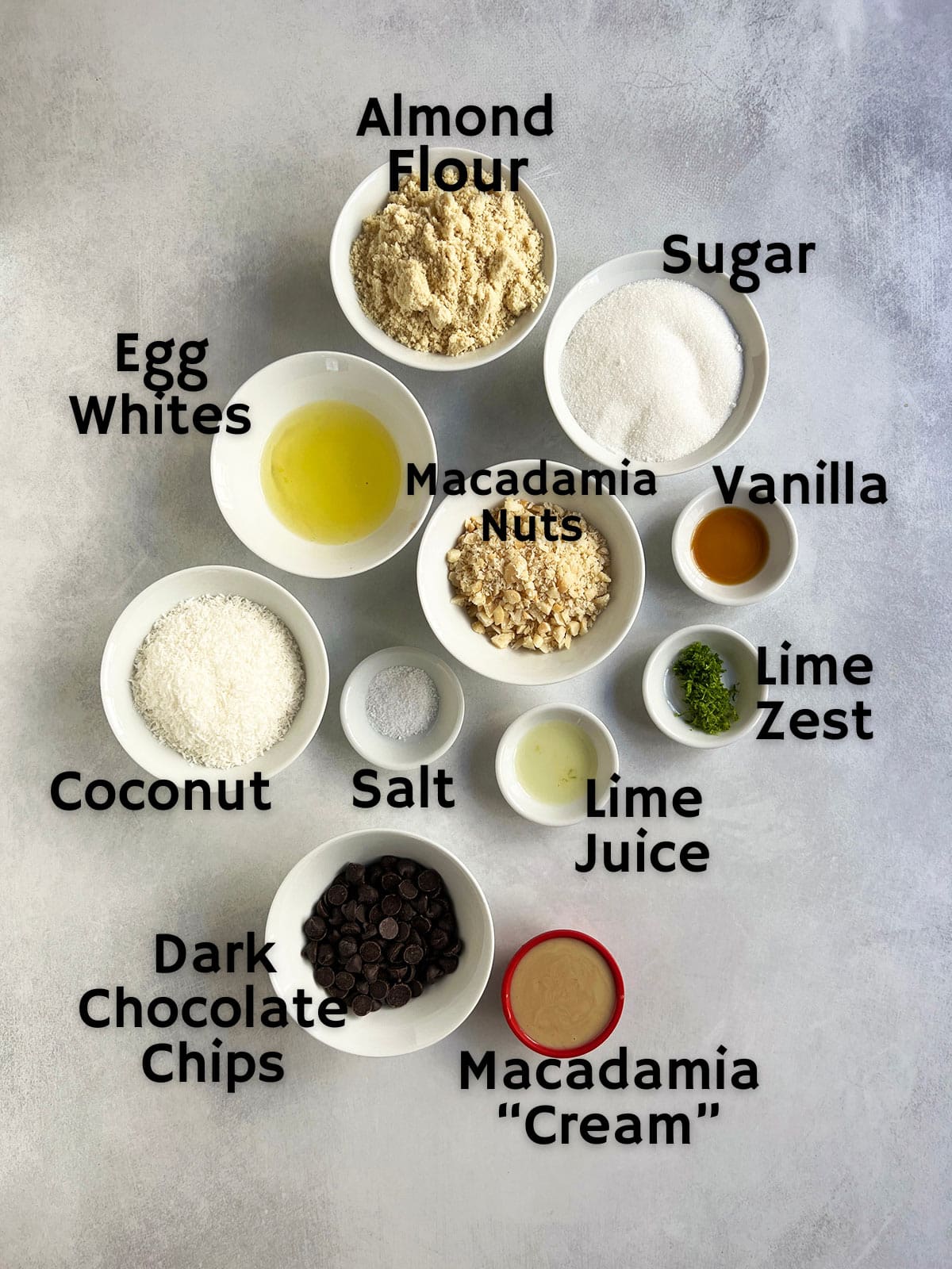 Ingredient shot for dairy-free macaroons showing all the ingredients in white bowls plus a red bowl with the optional macadamia cream in it.