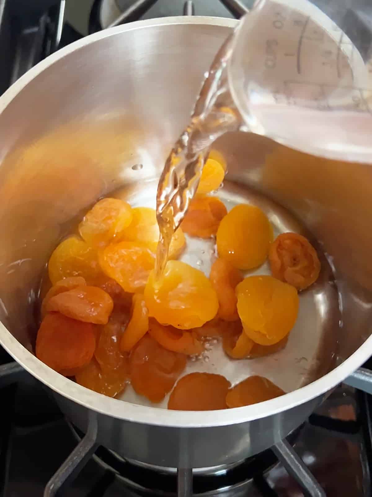 Pouring water over dried apricots in pot to begin process of making apricot filling.