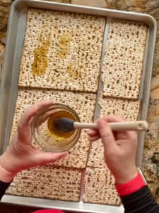 Beth brushing boards of matzo with flavored olive oil.