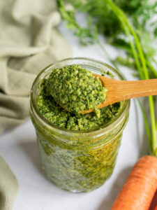 Preserved lemon pesto on a wooden spoon over a jar with carrot tops in the background.