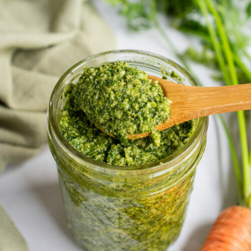 Preserved lemon pesto on a wooden spoon over a jar with carrot tops in the background.