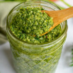Carrot top pesto in a jar with a close up on a wooden spoon with a dollop of pesto on it.
