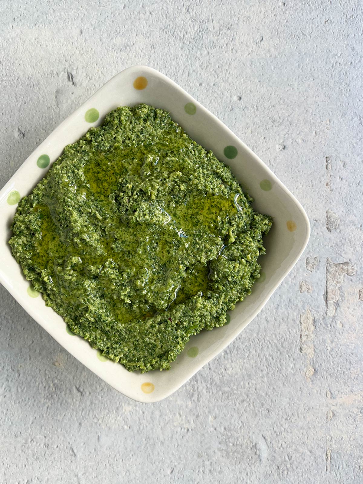 Carrot top, arugula, parsley pesto in a polka dot bowl with oil drizzled on top.