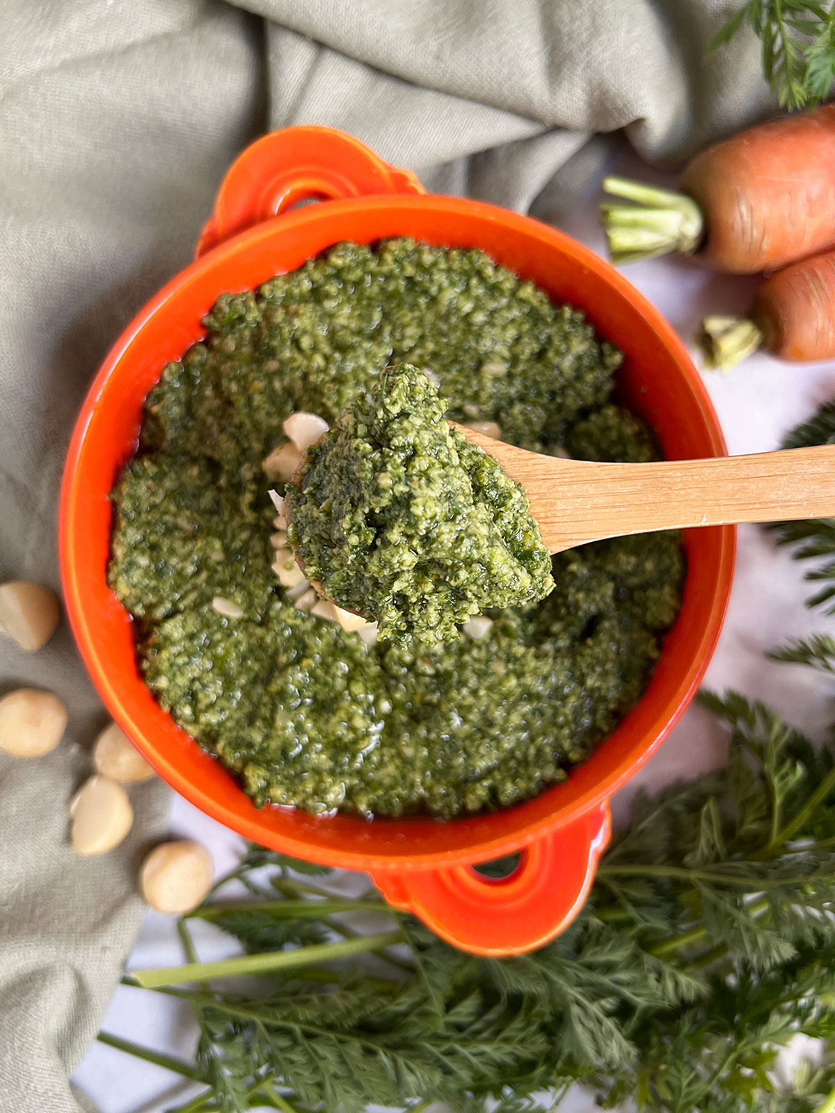 Macadamia nut pesto dolloped on a wooden spoon with an orange bowl of pesto in the background.
