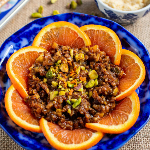Pomegranate charoset in a blue bowl with oranges surrounding it and pistachios on top.