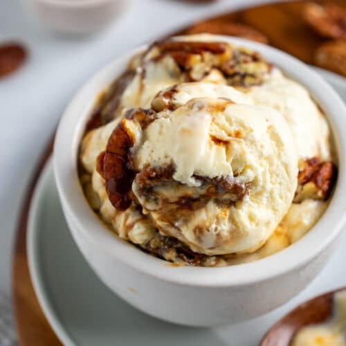 Butter pecan ice cream in an off white bowl with melty ice cream on a wooden spoon.