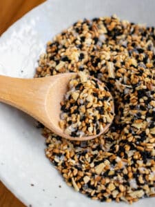 Everything bagel seasoning in a white bowl with a wooden spooful on top.