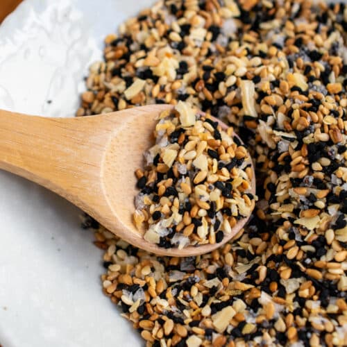 Everything bagel seasoning in a white bowl with a wooden spooful on top.