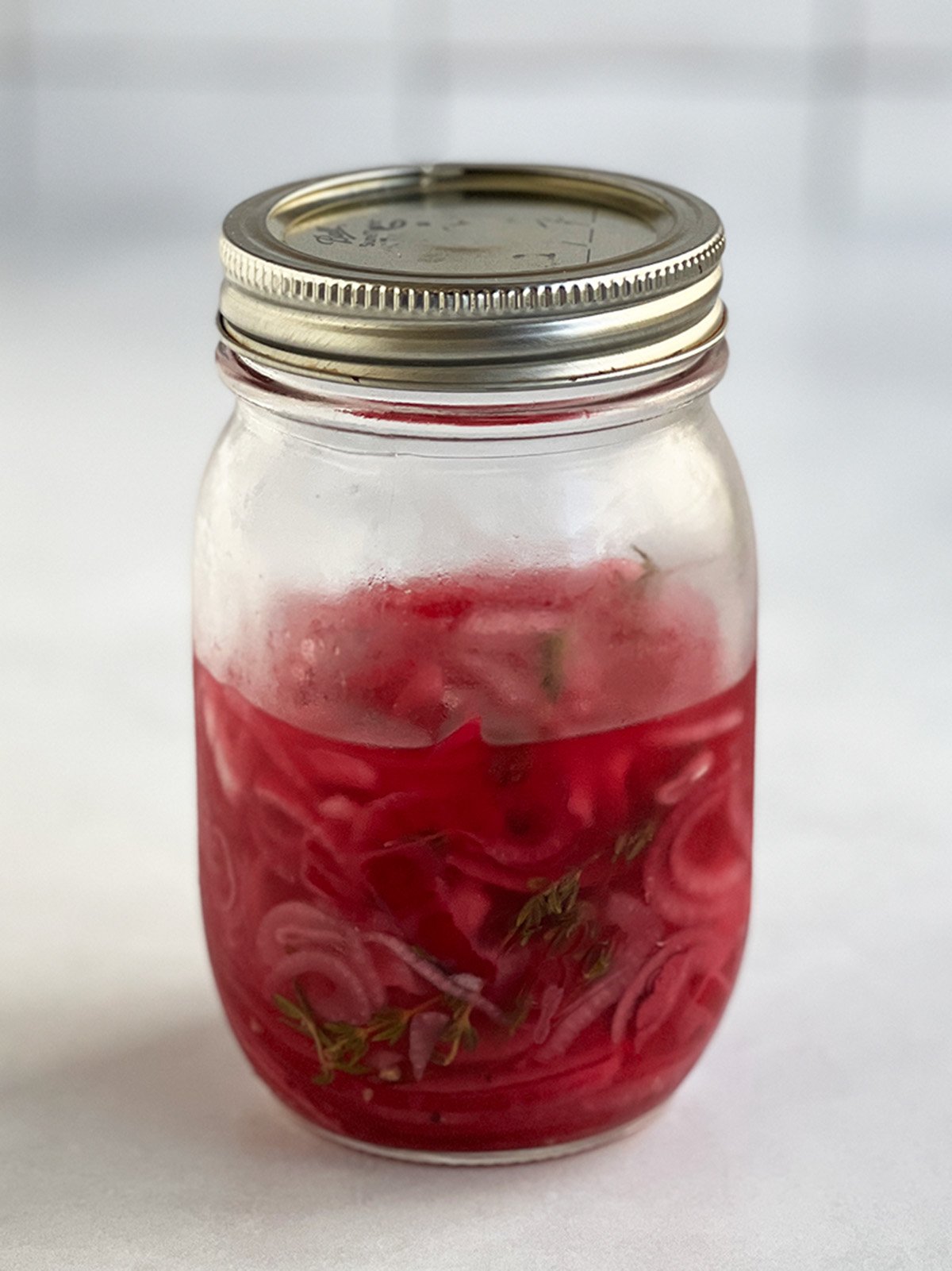 Pickled red onions ready to eat in a larger jar that looks about ⅔ full.