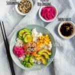 Ingredient shot for smoked salmon poke bowl showing a completed bowl on a striped napkin with side dishes of shoyu sauce, pickled red onions and everything bagel seasoning.