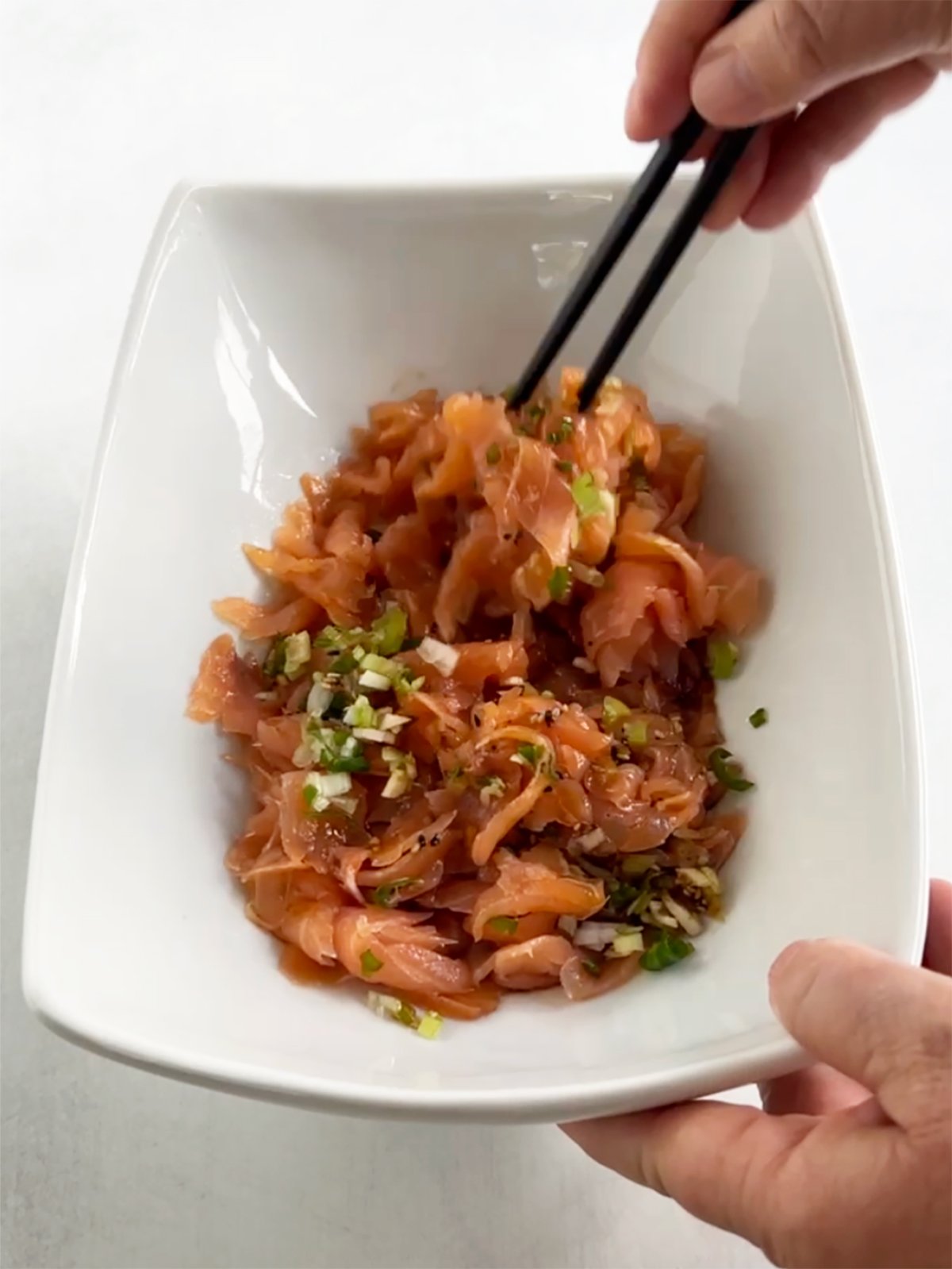 Beth mixing salmon and shoyu sauce with black chopsticks.