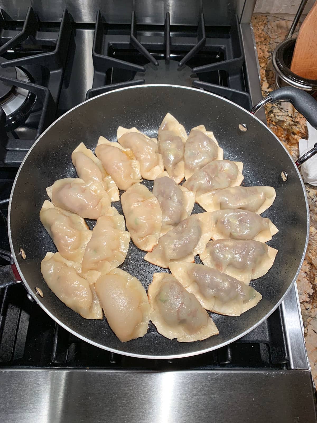 A large skillet filled with Korean kreplach pan frying and browning on one side.