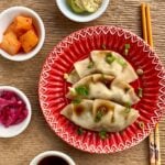 Beef dumpling on a red plate with orange chopsticks and four small white bowls on the side.