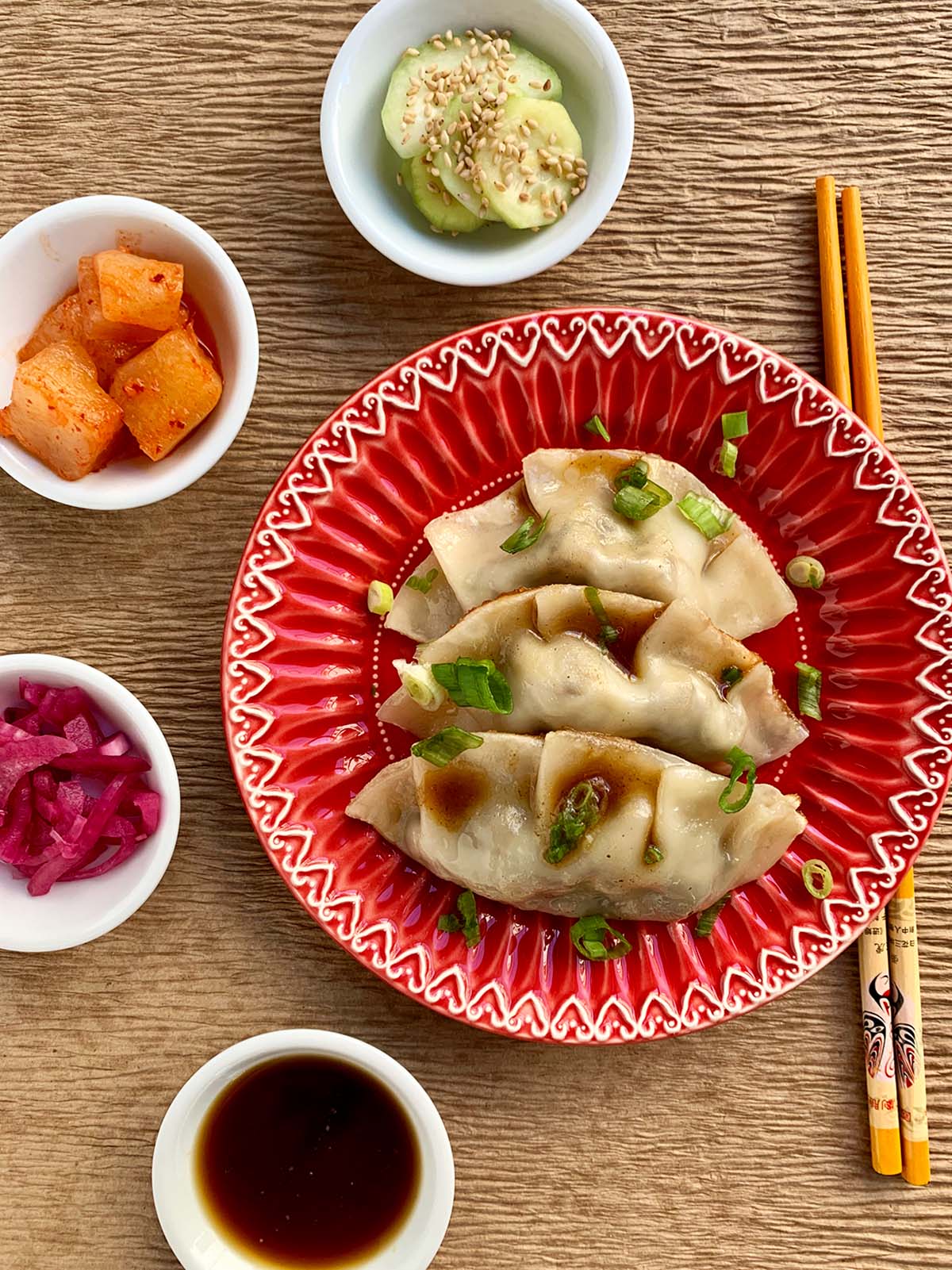 Beef dumpling on a red plate with orange chopsticks and four small white bowls on the side.