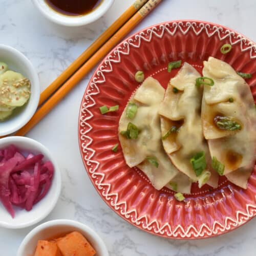 Korean beef dumplings or Jew Mandu on a red plate with chopsticks and hapa banchan on a marble table.